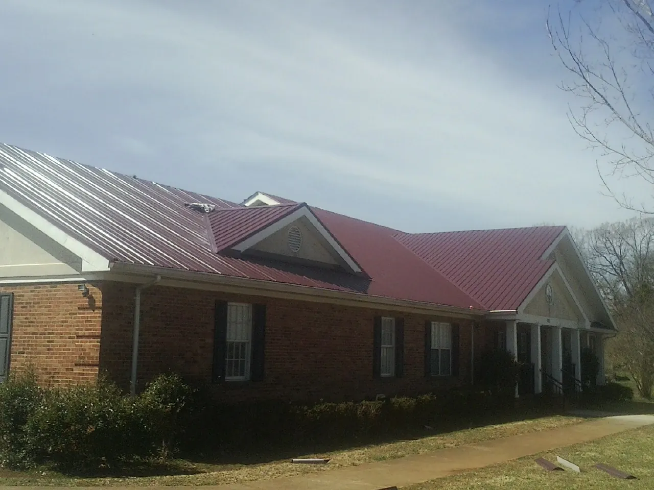 Red metal roof with gabled entries on a long brick building, from a Hail Damage Roof Repair job in Glyndon