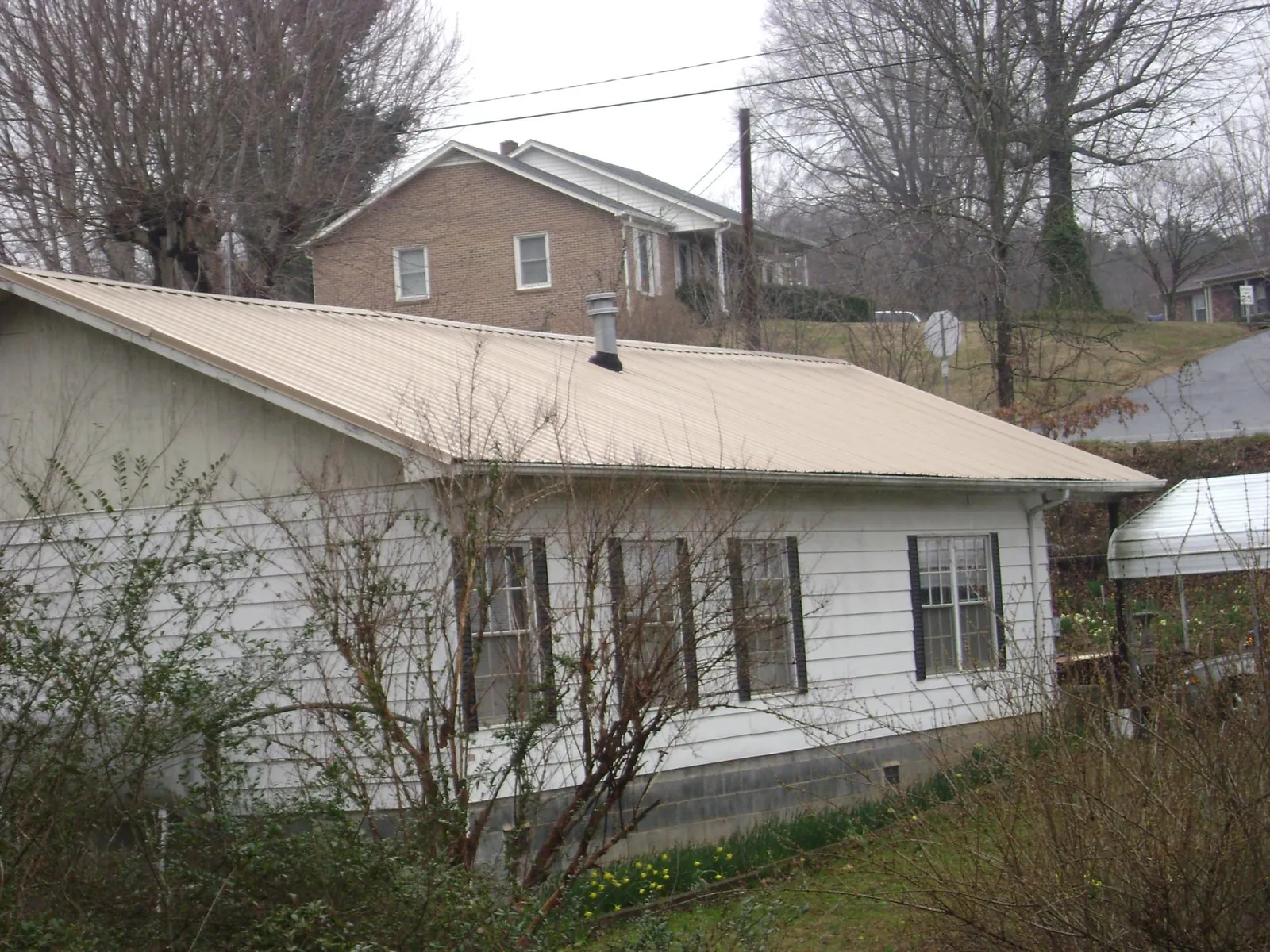 Tan metal roof on a white sided house set into a hillside — Commercial Roofing by Roofing Brothers in Glyndon